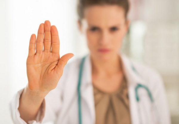 Женщина-врач вытягивает руку вперёд в знаке запрета
