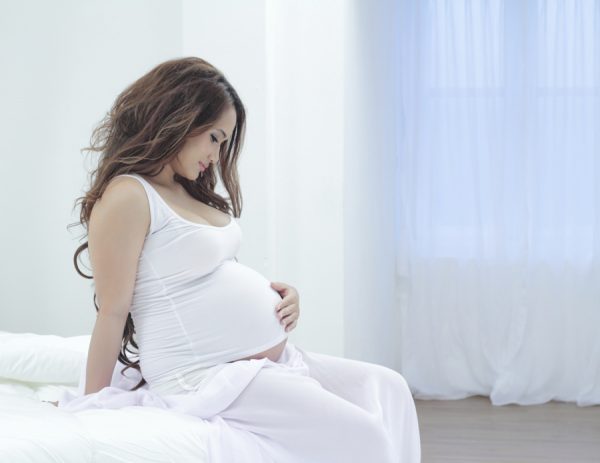 Беременная женщина сидит на кровати
