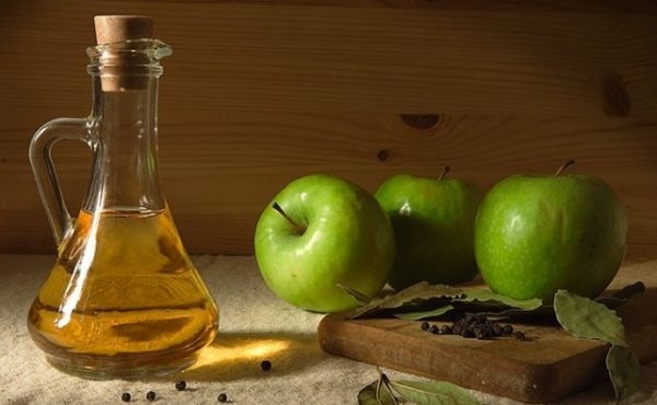 Яблочный уксус в прозрачном сосуде и плоды