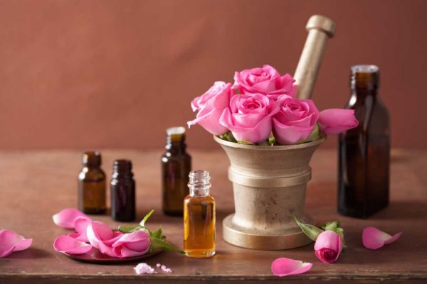 Эфирное масло розы в прозрачной бутылочке и цветы