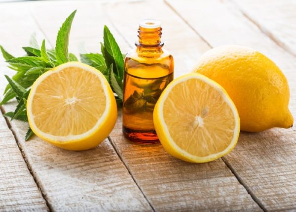 Лимонное масло в тёмном флаконе и плоды в разрезе