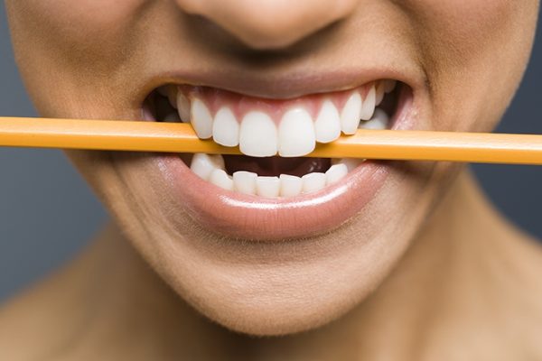Девушка держит карандаш между зубами